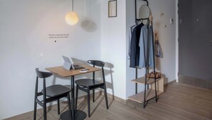 Une pièce moderne avec une table en bois, deux chaises, un ordinateur portable, une lampe suspendue et un porte-manteau avec des vêtements.