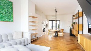 A modern living room with a sofa, a dining area with a table and chairs, and built-in wooden shelving. - Bright Duplex with Balcony in Antwerp (Antwerpen)