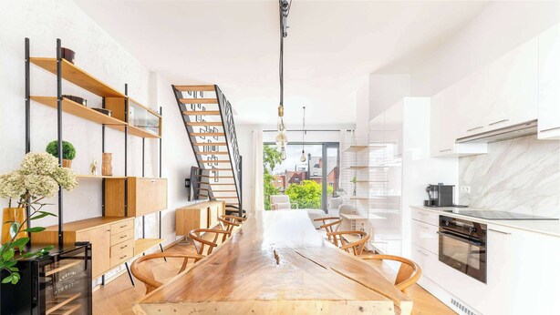 A modern kitchen with a central island, wooden chairs, and a built-in oven. - Bright Duplex with Balcony in Antwerp (Antwerpen)