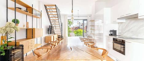 A modern kitchen with a central island, wooden chairs, and a built-in oven.