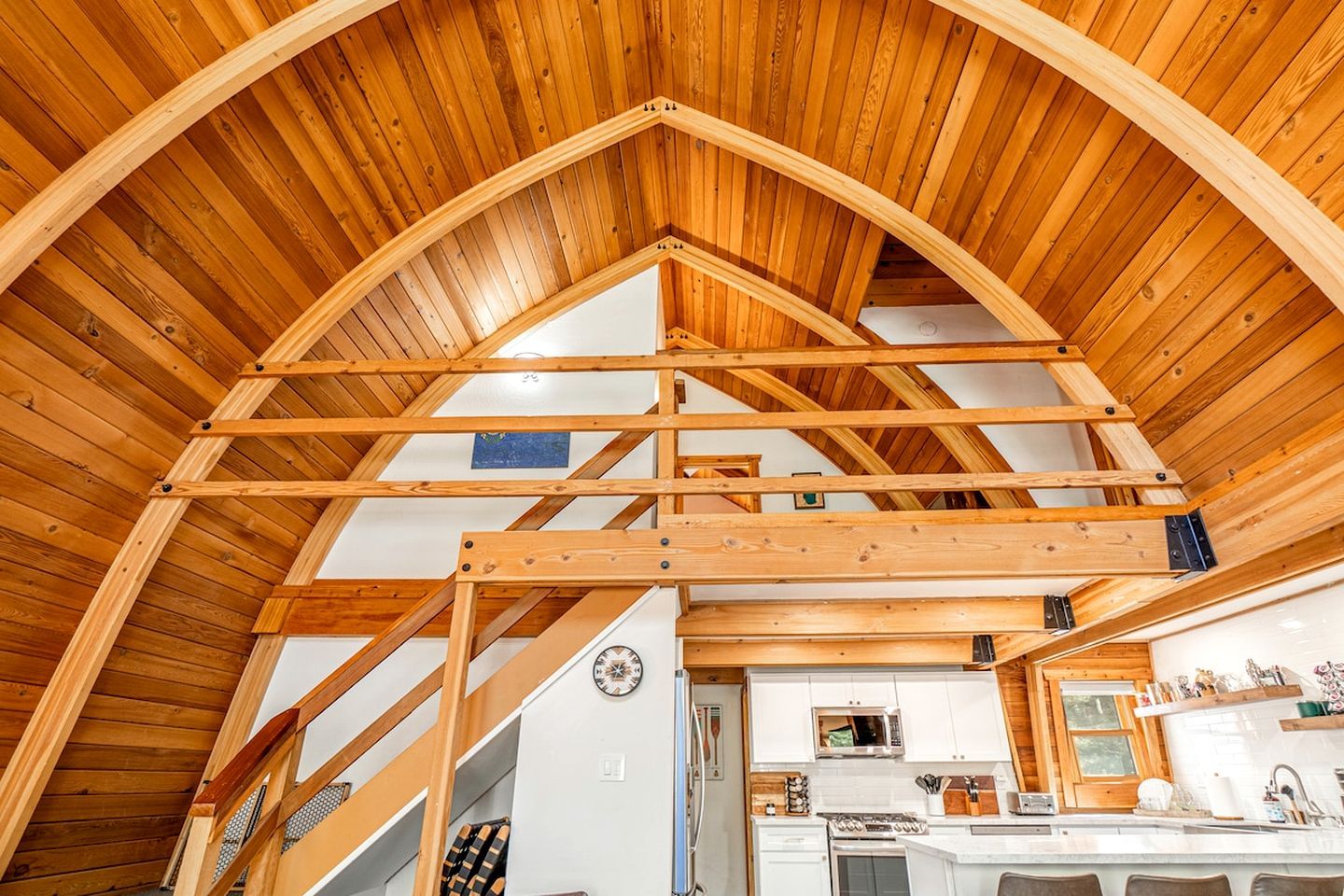 A wooden interior with a high ceiling and exposed beams, a kitchen area with modern appliances, and a staircase leading to an upper level.