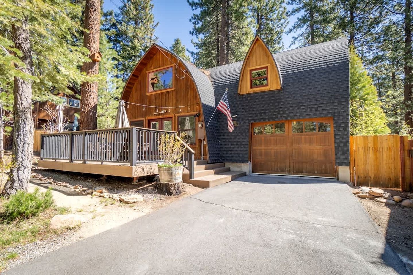 A cabin with a wooden deck, a garage, and a flag.
