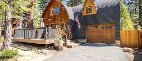 A cabin with a wooden deck, a garage, and a flag.