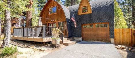 A cabin with a wooden deck, a garage, and a flag.