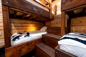 Yksinkertaisesti suunniteltu huone, jossa on puinen kerrossänky. Toisessa sängyssä on patja ja tyyny, ja toisessa on peitto.