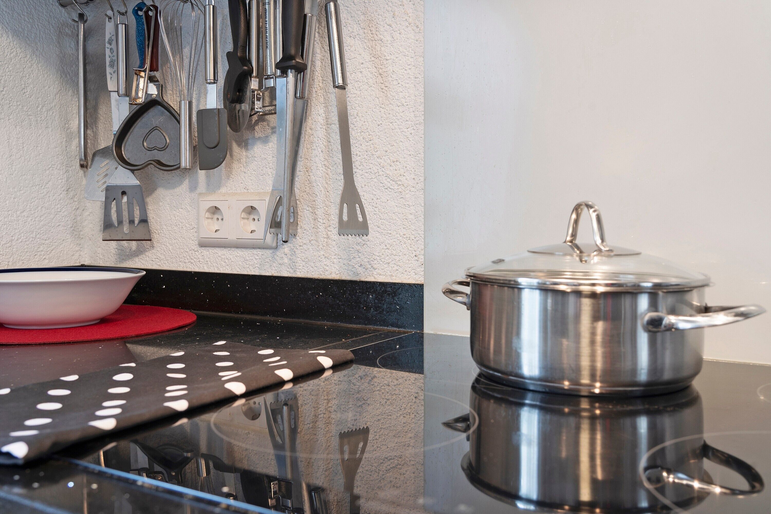 Une cuisine avec une casserole en acier inoxydable posée sur le comptoir, un tapis rouge et divers ustensiles de cuisine accrochés au mur.