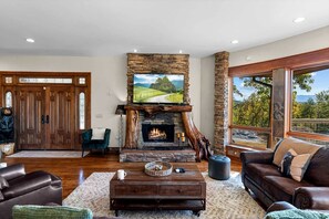 A living room with a stone fireplace, leather furniture, and a large window with a view. - Luxury Mountain Cabin with Hot Tub and Panoramic Views near Pigeon Forge, Tennessee (Sevierville)