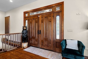 A wooden front door with glass panels, a bear sculpture, a staircase with a wooden railing, and a teal armchair. - Luxury Mountain Cabin with Hot Tub and Panoramic Views near Pigeon Forge, Tennessee (Sevierville)