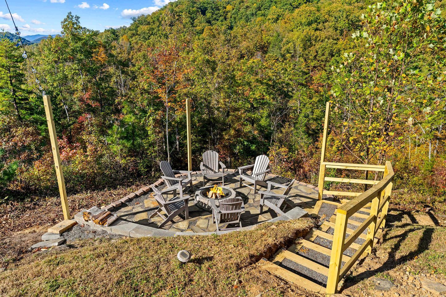 A circular outdoor seating area with Adirondack chairs, a fire pit, and a wooden fence.