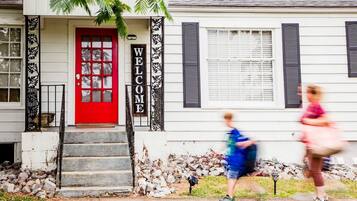 A house with a red door, a welcome sign, and a staircase leading to the entrance.