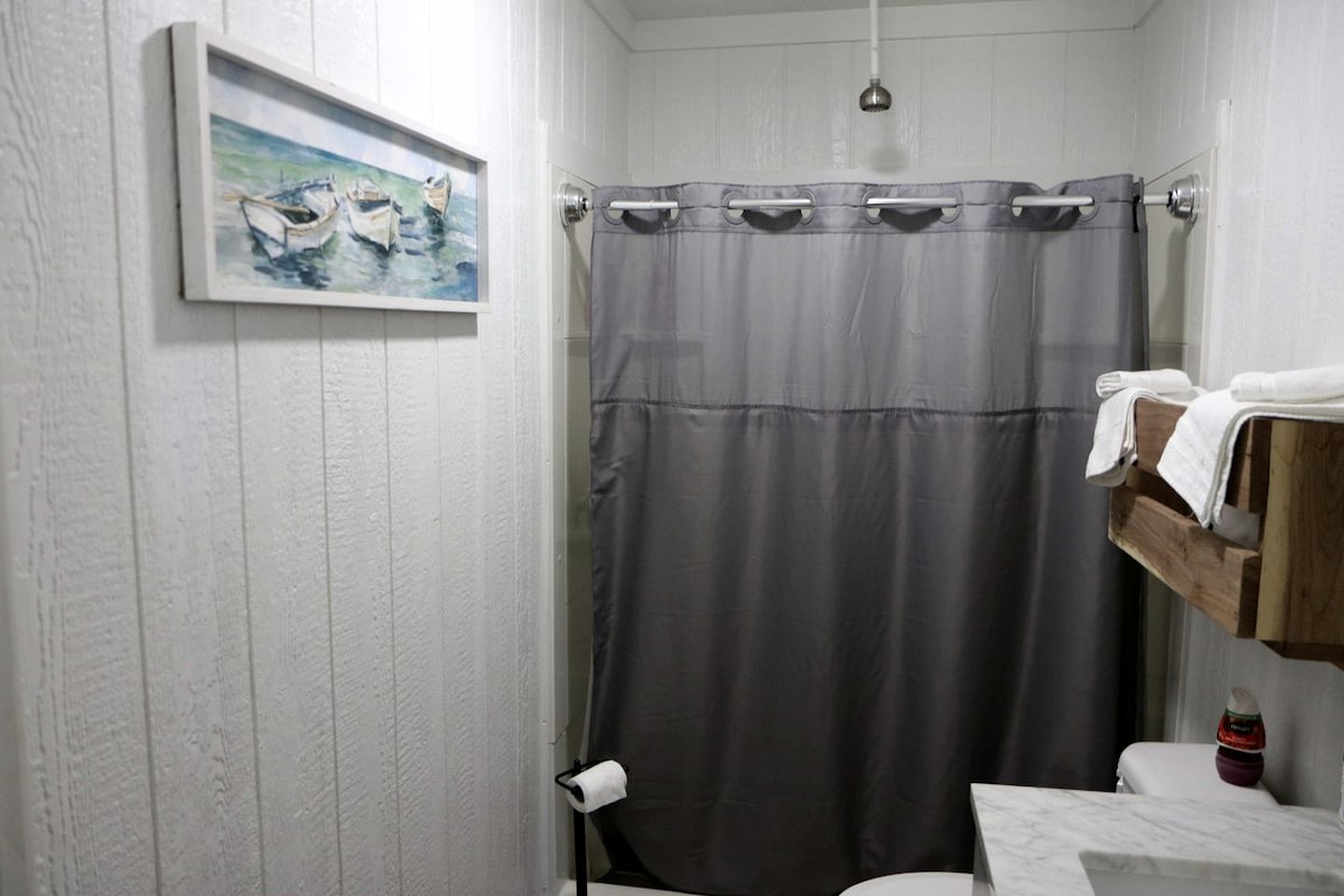 A bathroom with a shower curtain, a towel rack, a painting on the wall, and a toilet.