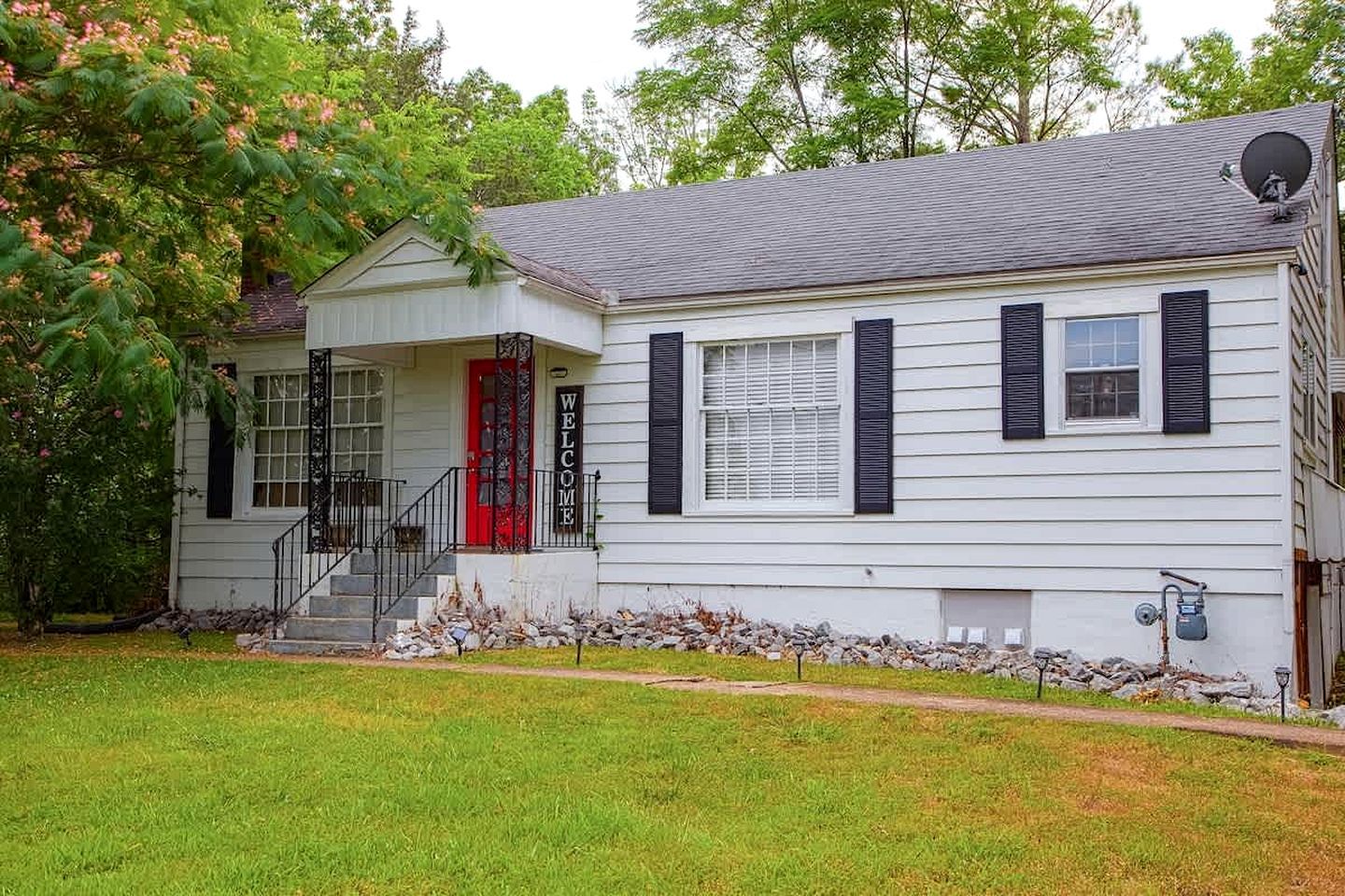 A two-story house with a red door, black shutters, and a 'WELCOME' sign.
