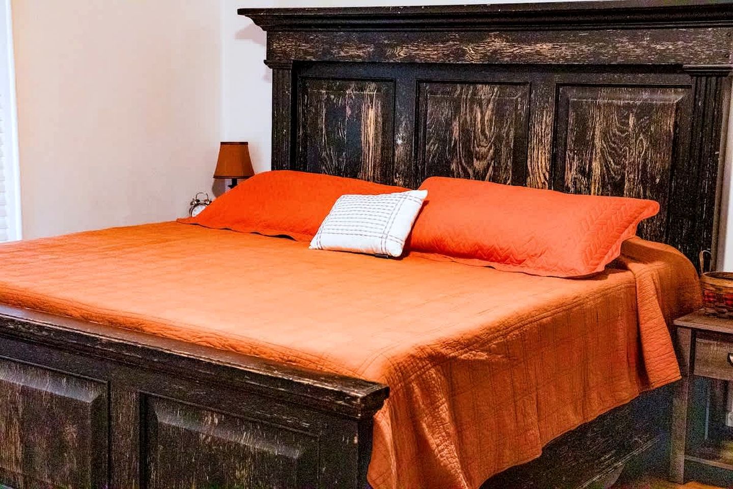 A bed with a dark headboard, a bright orange bedspread, and a white pillow.