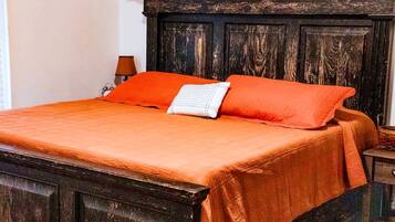 A bed with a dark headboard, a bright orange bedspread, and a white pillow.