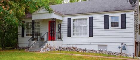 A two-story house with a red door, black shutters, and a 'WELCOME' sign.