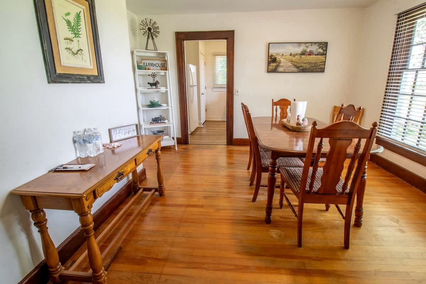 A dining area with a wooden table and chairs, a bookshelf, and a painting on the wall.
