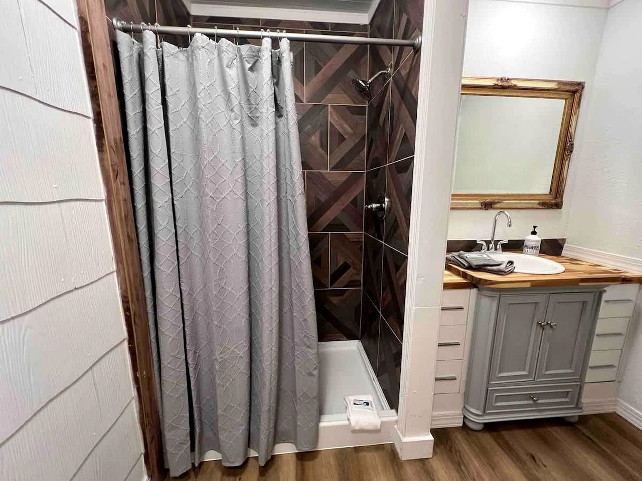 A bathroom with a shower curtain, a sink, a mirror, and a cabinet.