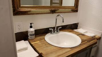 A bathroom with a wooden vanity, a white sink, a mirror with a gold frame, a bottle of hand soap, and a towel.