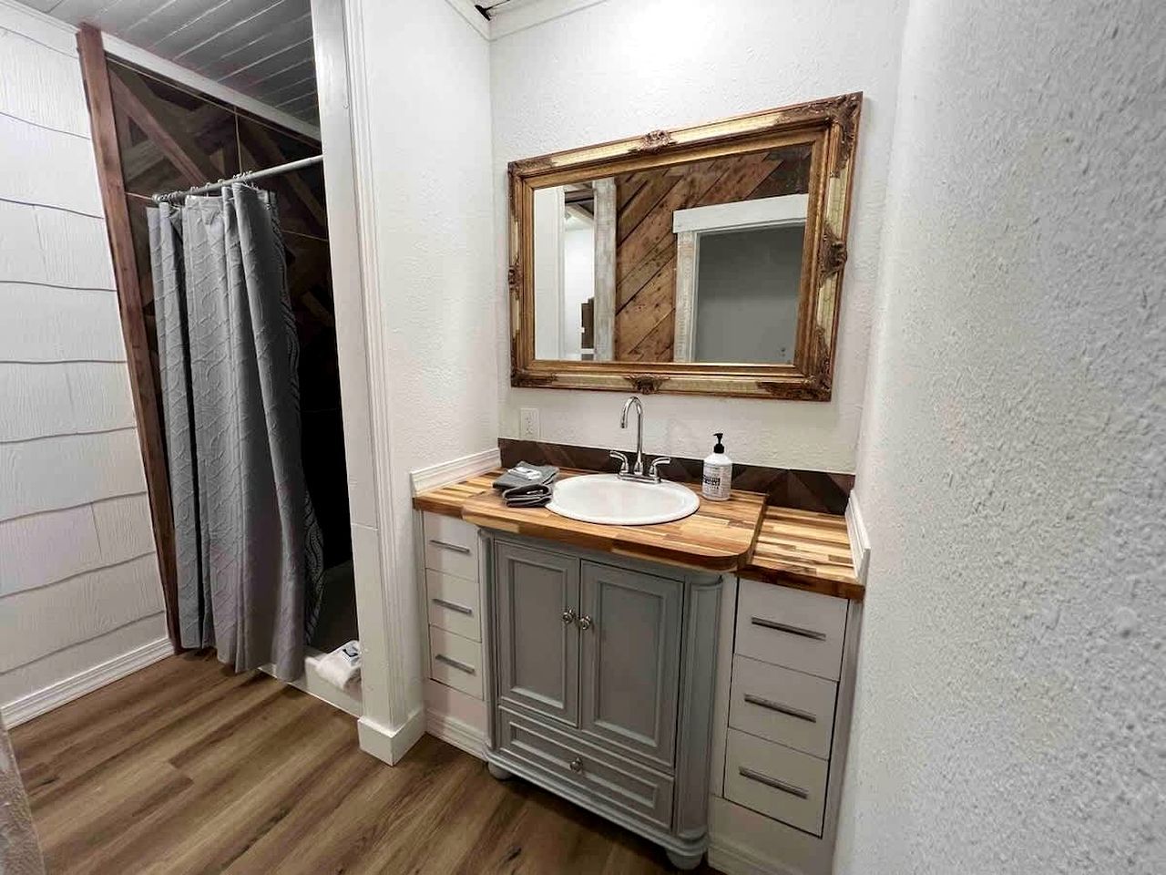 Une salle de bain avec un meuble-lavabo en bois, un lavabo blanc, un miroir avec un cadre en bois et un rideau de douche.