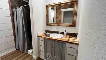 Une salle de bain avec un meuble-lavabo en bois, un lavabo blanc, un miroir avec un cadre en bois et un rideau de douche.