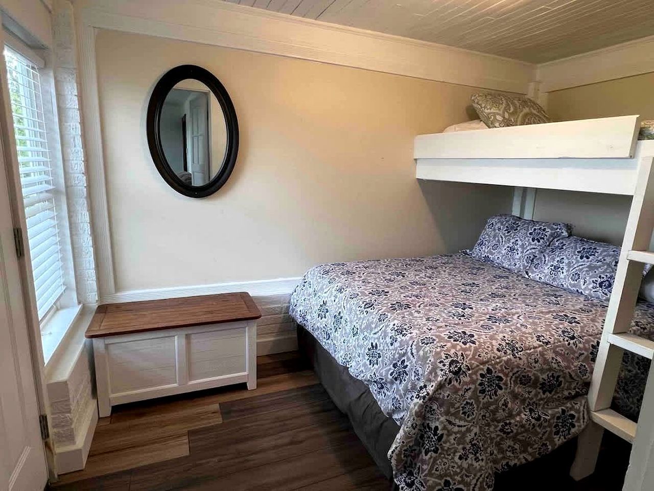 A bedroom with a bed, a bench, a mirror, and a window.