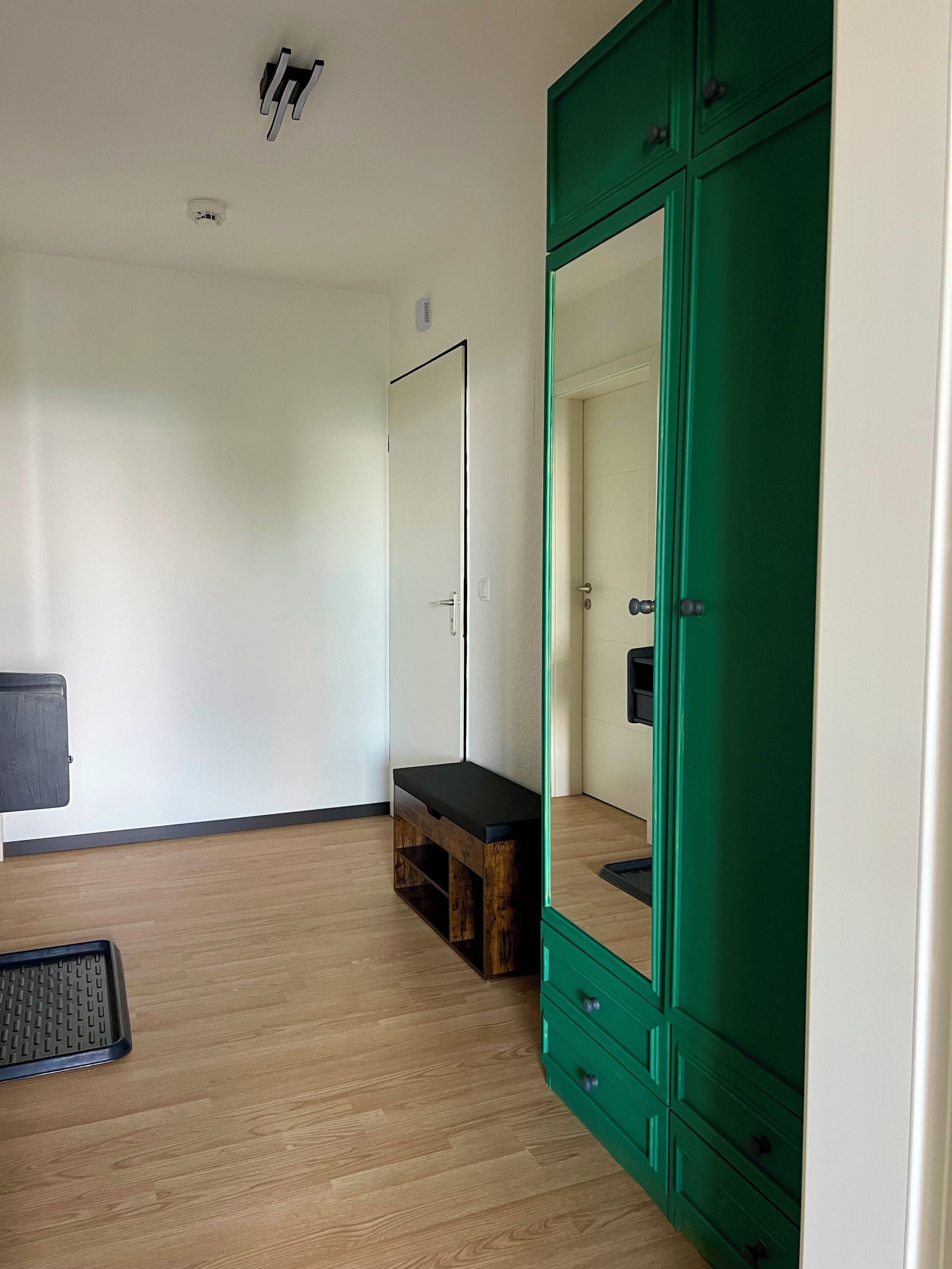 A room with a wooden floor, a bench, a green wardrobe, and a mirror.