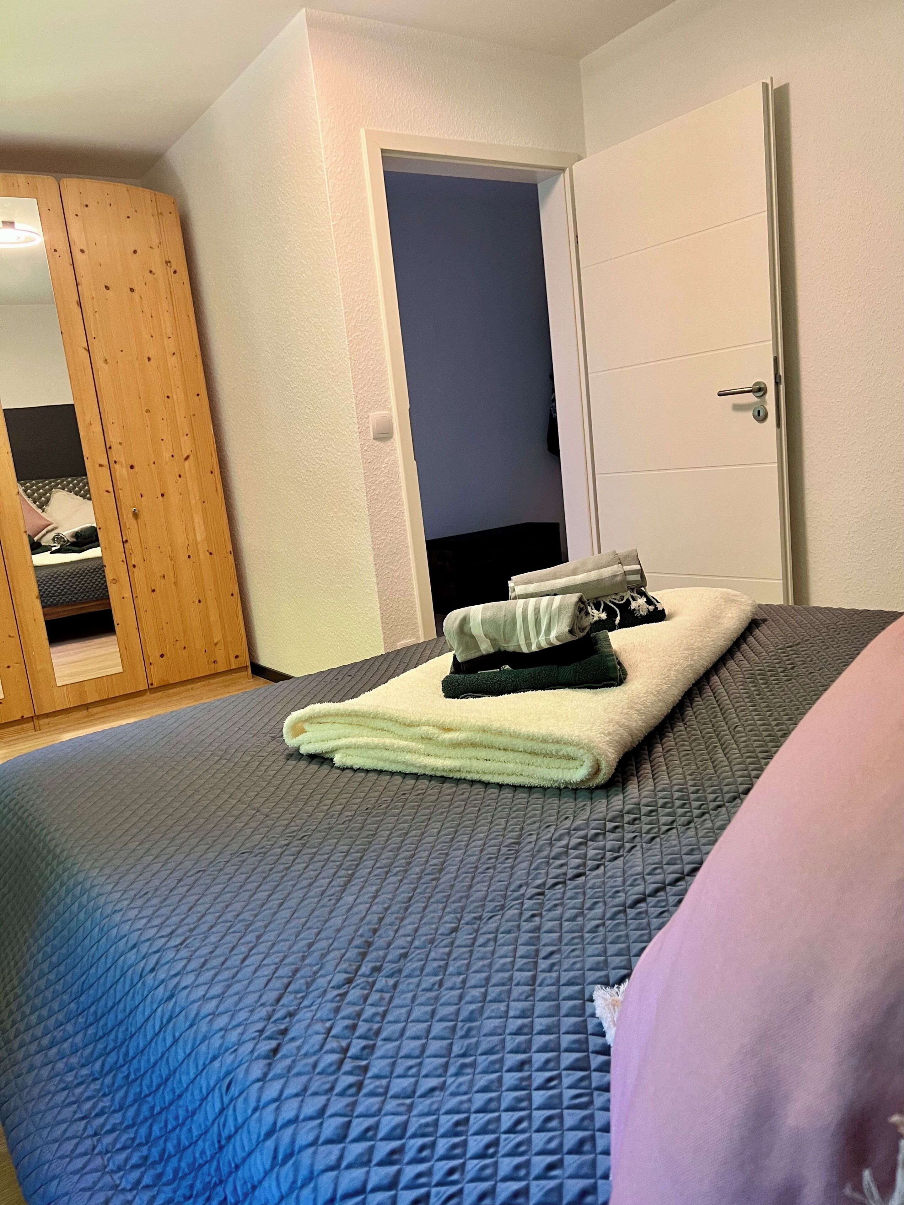 Een slaapkamer met een bed, een houten garderobe en een deur naar een andere kamer.