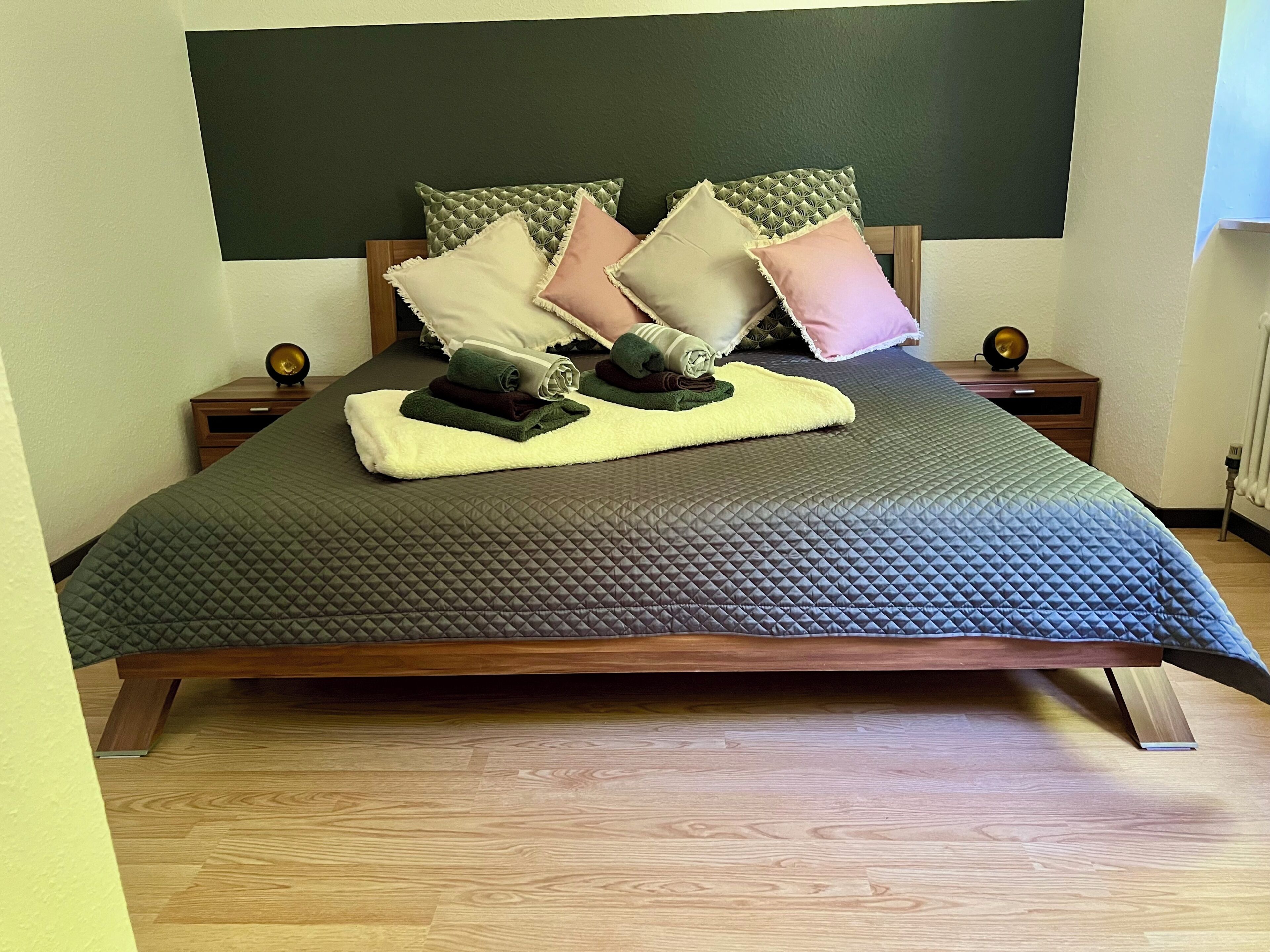 A bed with a quilted bedspread, pillows, a blanket, and a small table with a lamp.