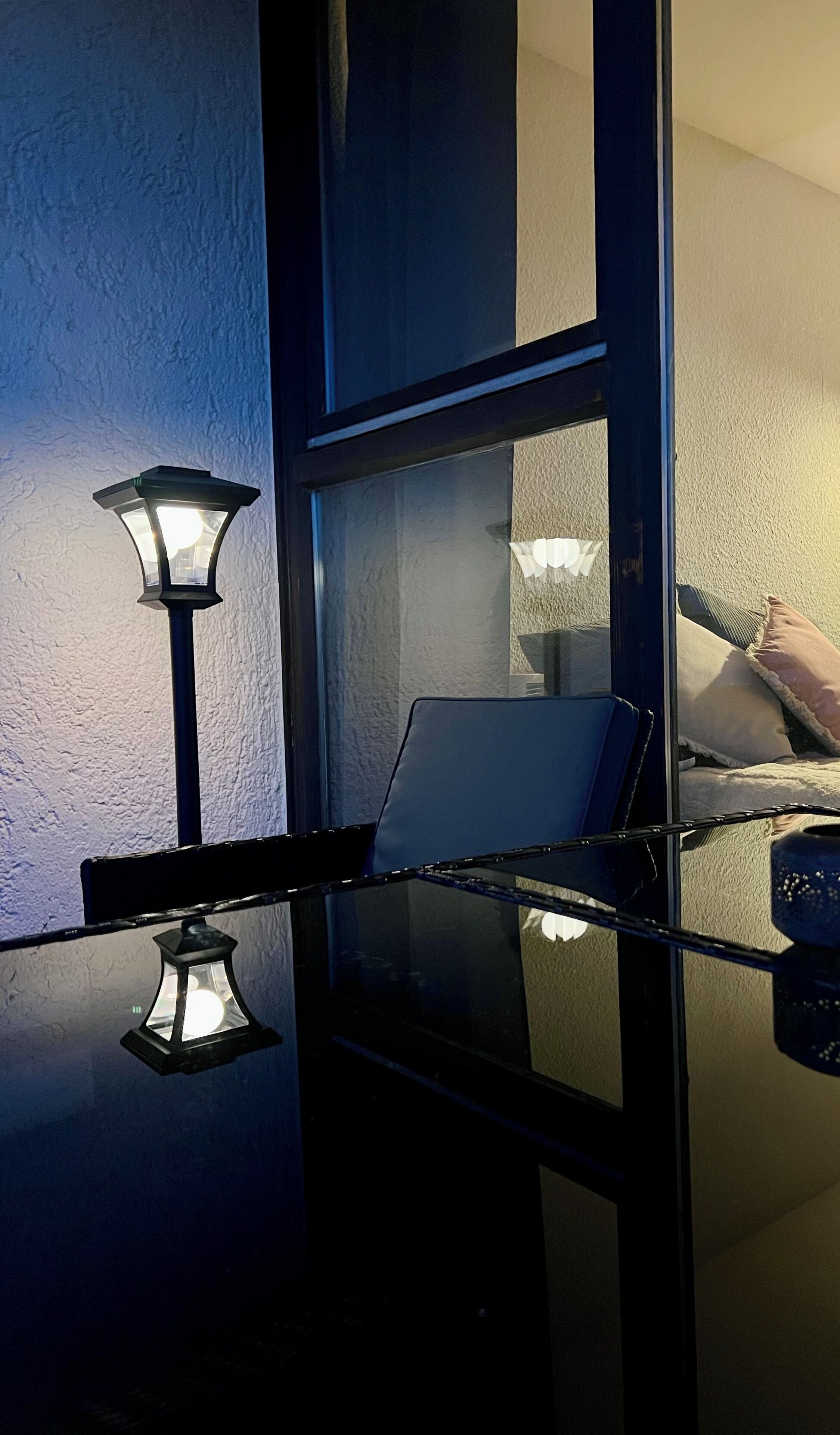 Una stanza con una parete divisoria in vetro, una lampada e il riflesso di un letto con cuscini.