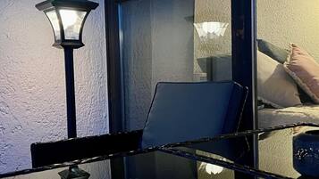 Una stanza con una parete divisoria in vetro, una lampada e il riflesso di un letto con cuscini.