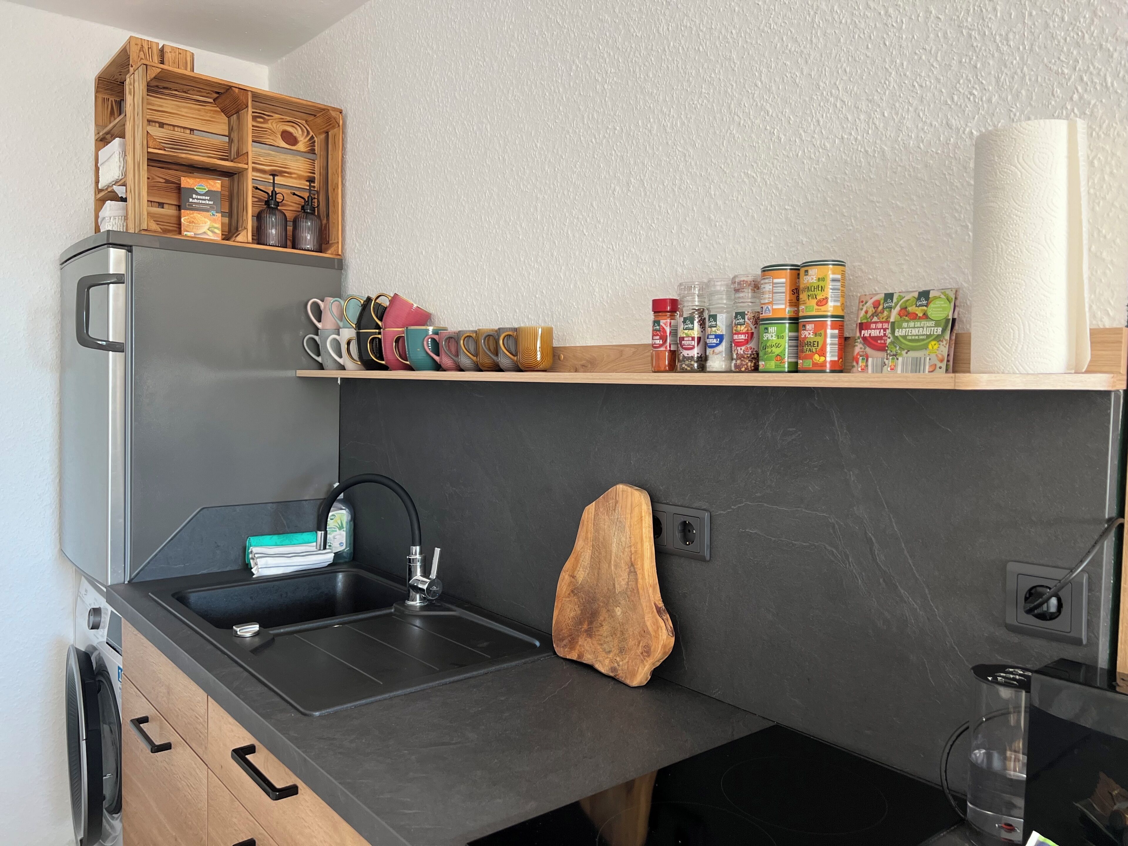 Una cocina moderna con un lavaplatos integrado, estantes de madera con especias y una cafetera.