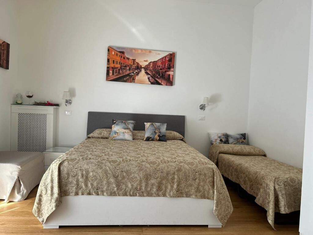 A bedroom with a large bed, two smaller beds, a nightstand, a lamp, and a wall-mounted picture.