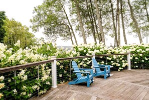 A wooden deck with two blue chairs and a white railing, surrounded by white flowers and trees.