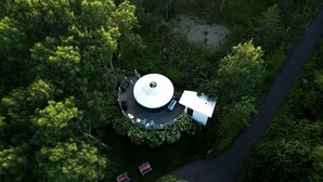 An aerial view of a circular building surrounded by dense greenery, with a paved path leading to it. - Romantic Luxury Yurt with Private Beach & Steam Shower near Friendship, Maine (Friendship)