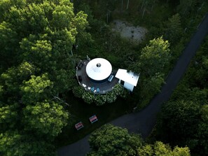 An aerial view of a circular building surrounded by dense greenery, with a paved path leading to it. - Romantic Luxury Yurt with Private Beach & Steam Shower near Friendship, Maine (Friendship)