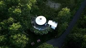 Vista aérea de um edifício circular rodeado por vegetação densa, com um caminho pavimentado a levar até ele.