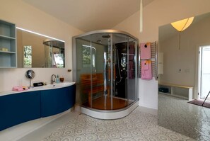 A modern bathroom with a glass-enclosed shower, a vanity with a mirror, and a patterned floor. - Romantic Luxury Yurt with Private Beach & Steam Shower near Friendship, Maine (Friendship)