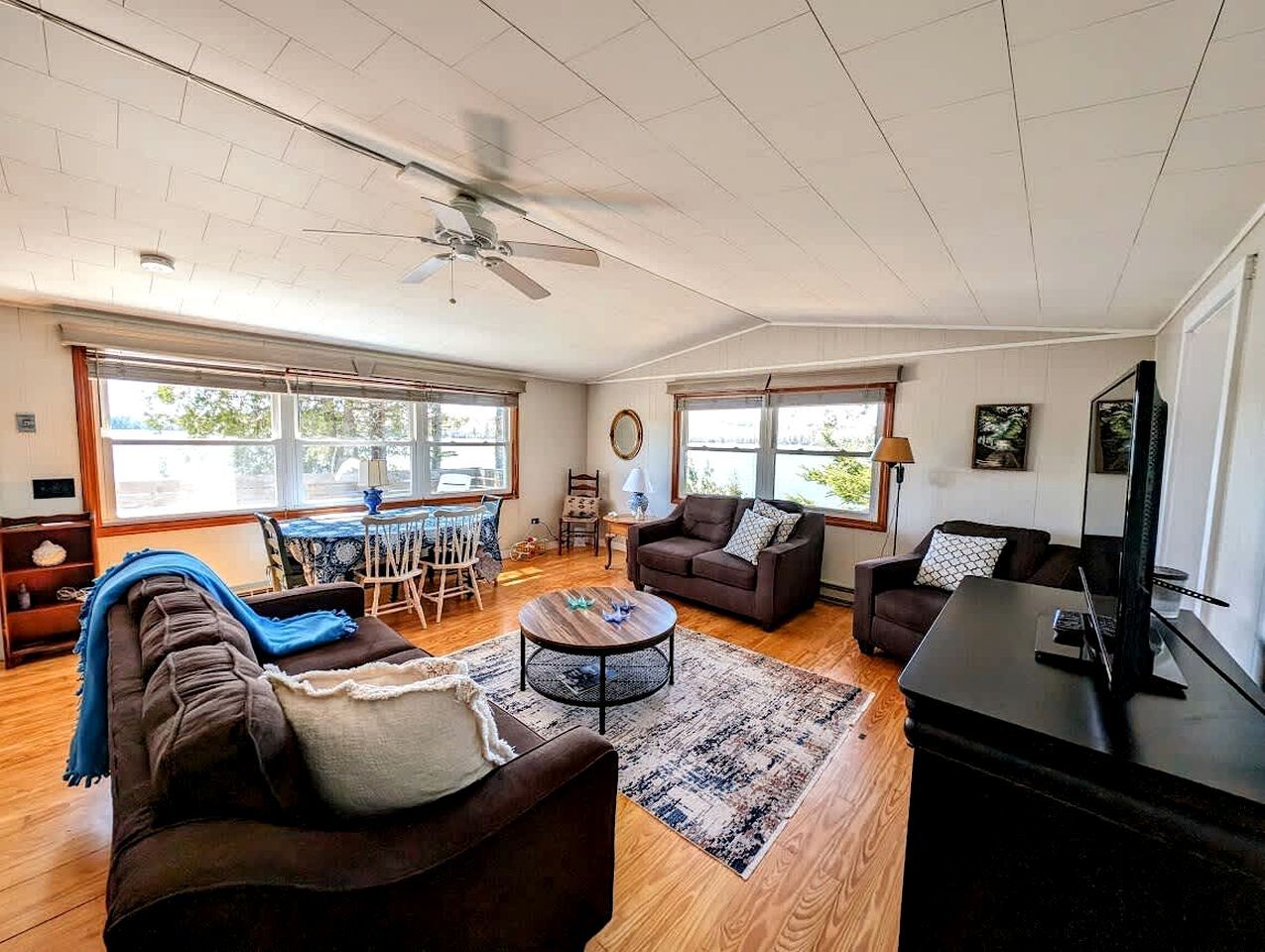 A spacious living room with a ceiling fan, large windows, a dining area, and a black entertainment unit.