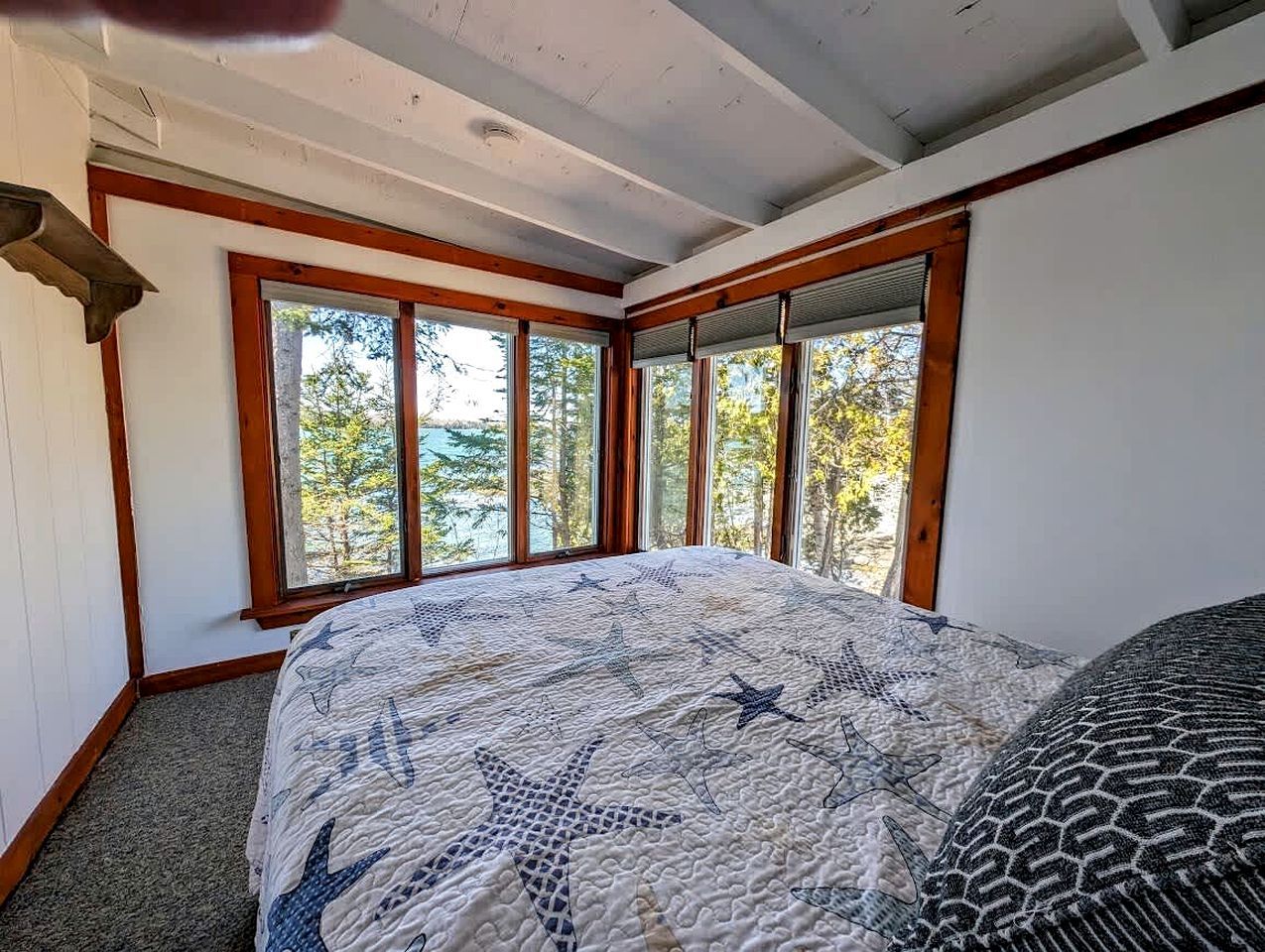 Un dormitorio con una cama grande, varias ventanas y vistas a árboles.