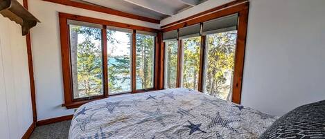 Un dormitorio con una cama grande, varias ventanas y vistas a árboles.