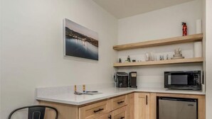 A compact kitchen with wooden cabinets, a stainless steel refrigerator, a microwave, and a coffee maker on a white countertop.