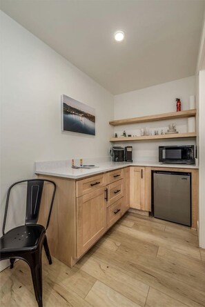A compact kitchen with wooden cabinets, a stainless steel refrigerator, a microwave, and a coffee maker on a white countertop.