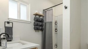 A modern bathroom with a wooden vanity, a shower with a grey curtain, and a window above the sink.
