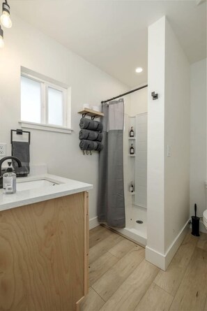 A modern bathroom with a wooden vanity, a shower with a grey curtain, and a window above the sink.
