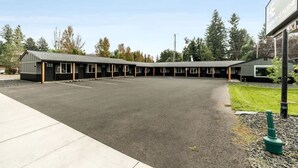 A motel with a row of rooms, a parking lot, and a grassy area with trees.