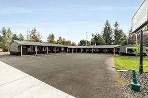 A motel with a row of rooms, a parking lot, and a grassy area with trees.