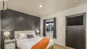 A modern bedroom with a bed, nightstands, a window, and a door.