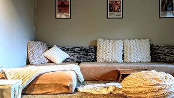 Een gezellige kamer met een bank, kussens, een plaid en een klein houten tafeltje.
