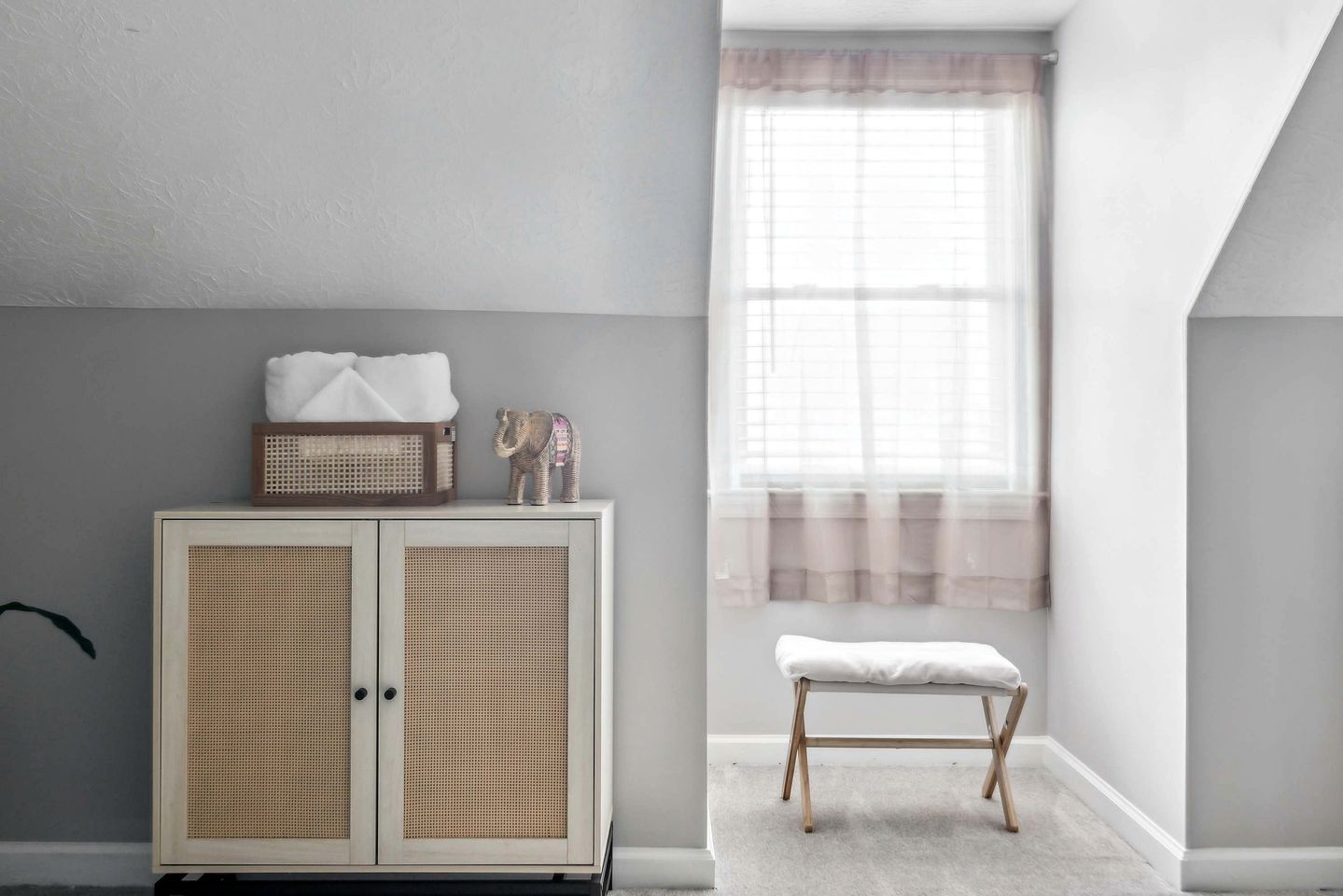 A room with a white cabinet, a bench, and a window with sheer curtains.