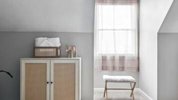 A room with a white cabinet, a bench, and a window with sheer curtains.